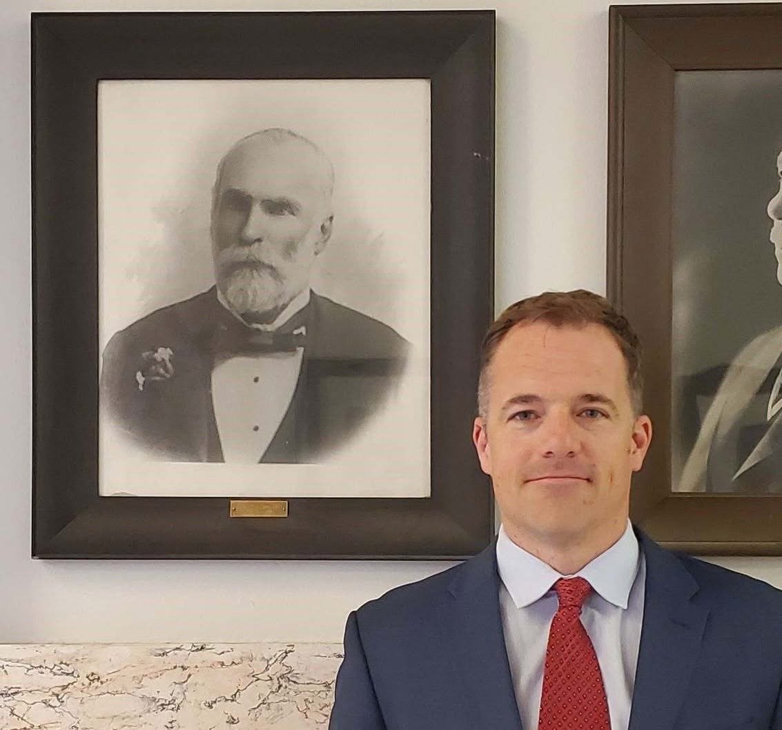 Ole Olson standing beneath the framed portrait of Judge William J. Galbraith in a Butte courthouse hallway